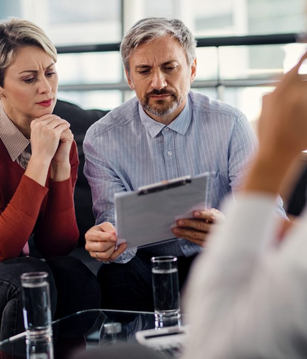 Mid adult couple analyzing terms of a contract while having a meeting with financial consultant in the office.